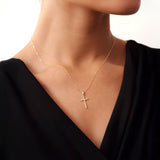 Luxury fashion editorial shot of a model wearing a small 14K solid gold cross necklace.