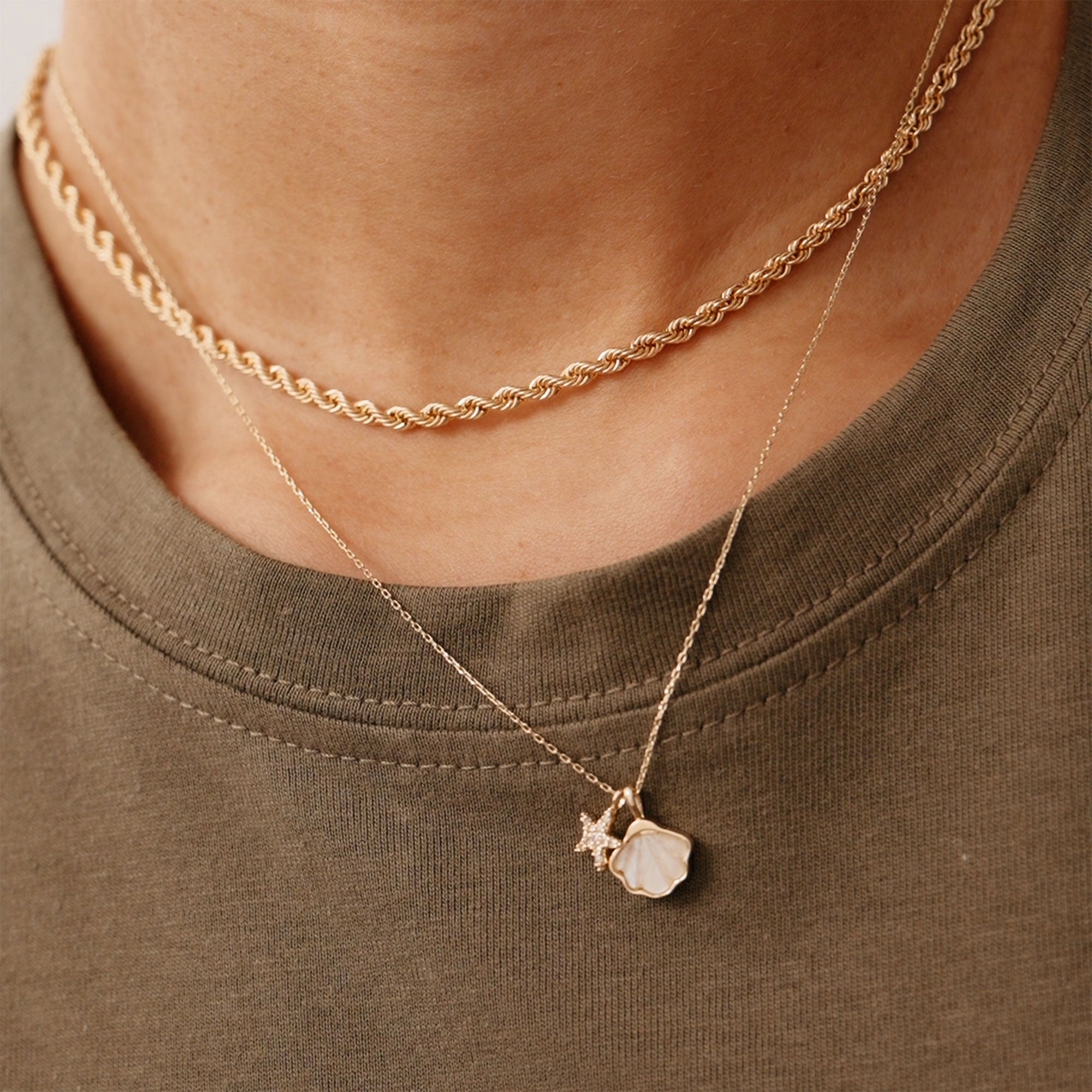 Close-up of a 14K yellow gold necklace with a mother-of-pearl seashell charm and diamond-encrusted starfish pendant. A stunning ocean-inspired piece of jewelry, ideal for layering or wearing solo, capturing the beauty of the sea.