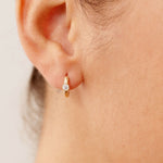 Elegant 14K yellow gold huggie earrings with bezel-set diamonds. The medium-sized hoops offer a delicate, minimalist design, perfect for layering or wearing alone as a statement piece for both casual and formal occasions.