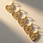 Five 14K solid gold personalized heart necklaces with initials M, S, A, E, and K, featuring a luxury sunburst texture on a white background.