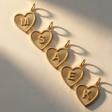 Five 14K solid gold personalized heart necklaces with initials M, S, A, E, and K, featuring a luxury sunburst texture on a white background.
