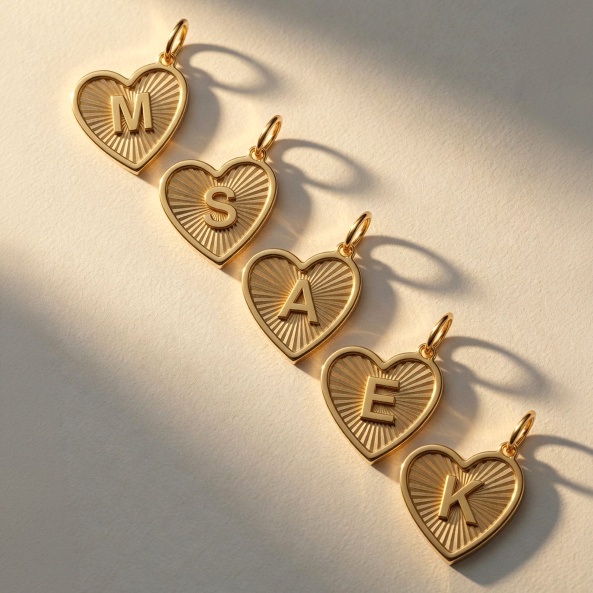 Five 14K solid gold personalized heart necklaces with initials M, S, A, E, and K, featuring a luxury sunburst texture on a white background.