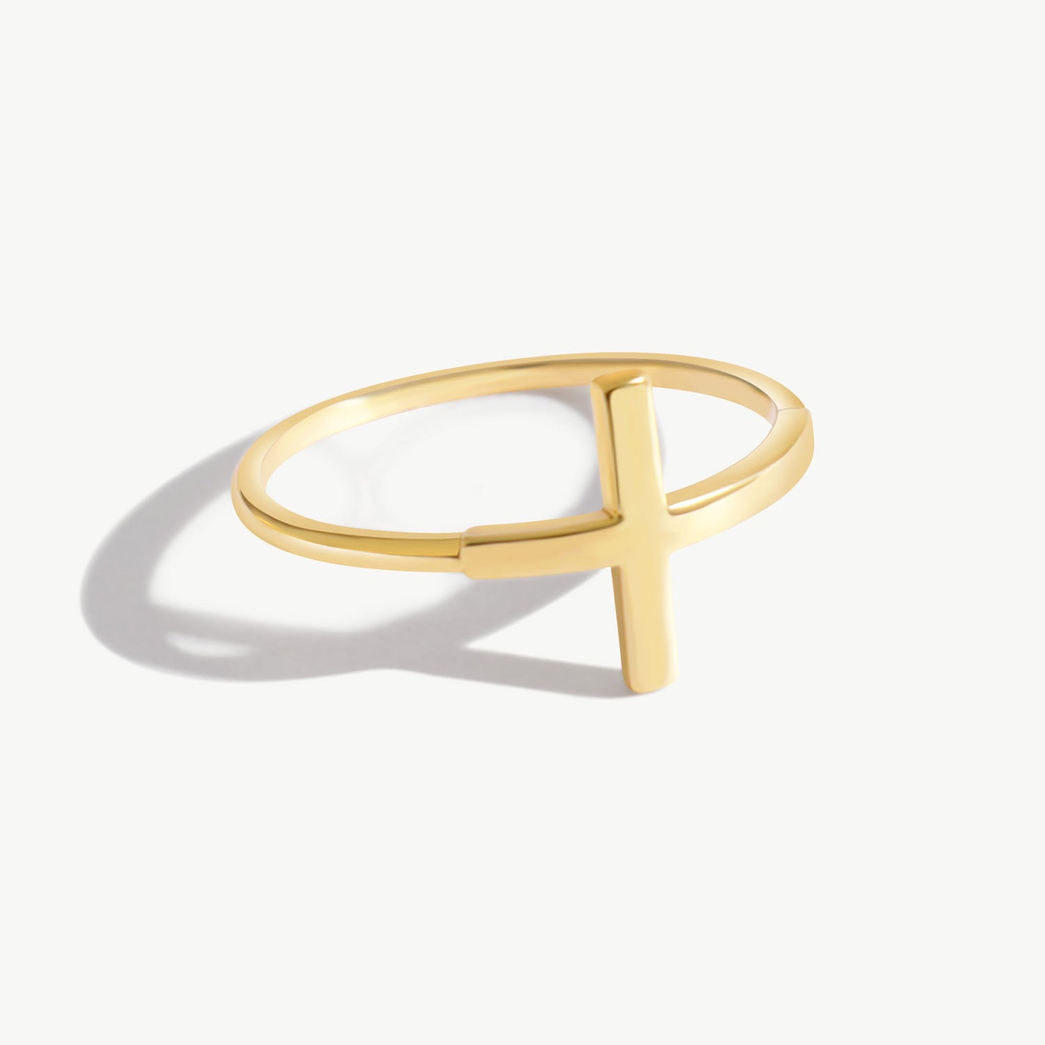 Minimalist 14K solid yellow gold cross ring with a sleek modern cross silhouette photographed on a clean white background, featuring a delicate polished band and soft natural shadow reflection.
