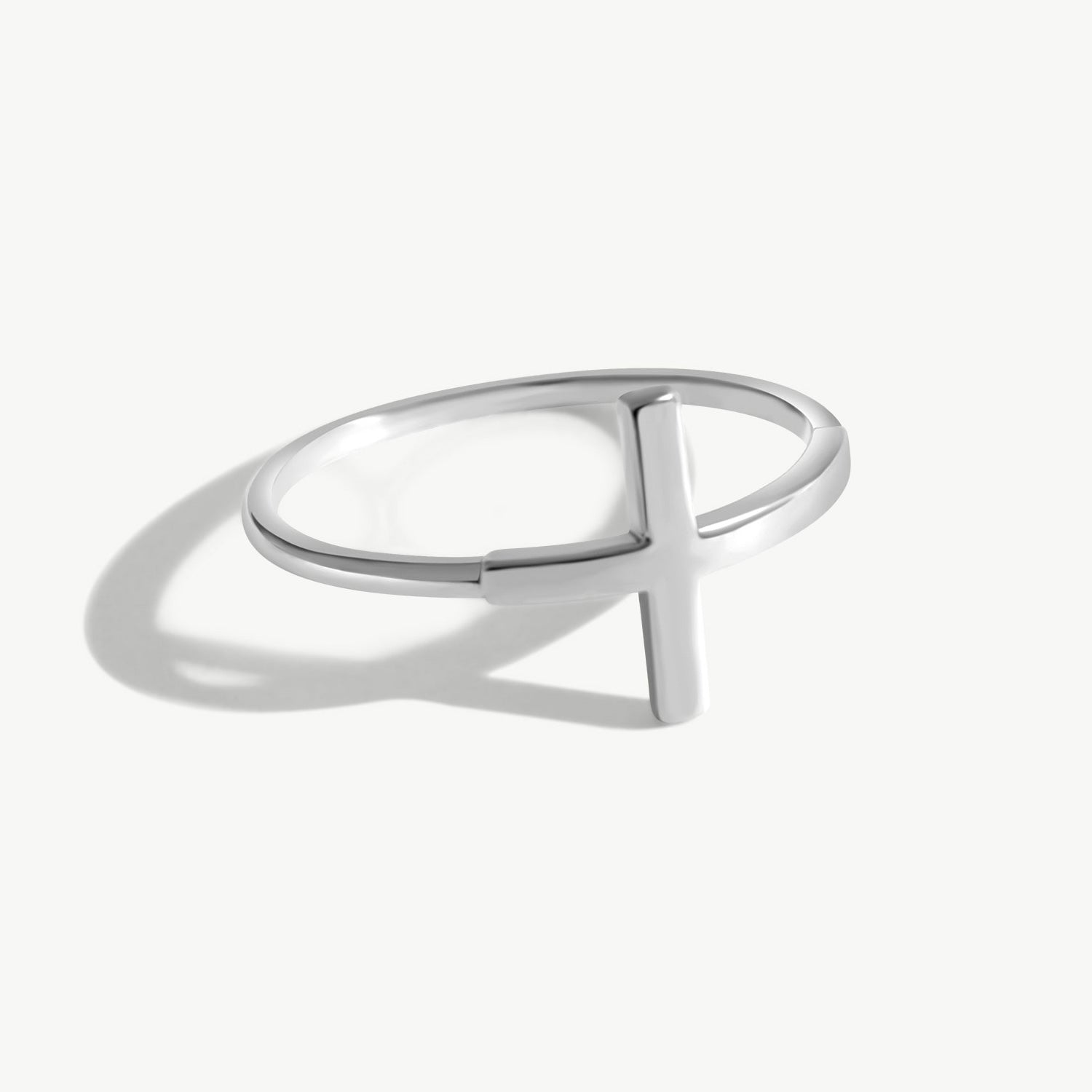 14K solid white gold cross ring photographed on a white background with realistic reflections and shadowing, featuring a minimalist sideways cross design and thin polished band suitable for stacking.