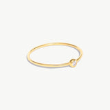 Side-angle product photograph of a delicate 14K solid gold birthstone ring with natural diamond bezel setting and ultra-thin minimalist band design.