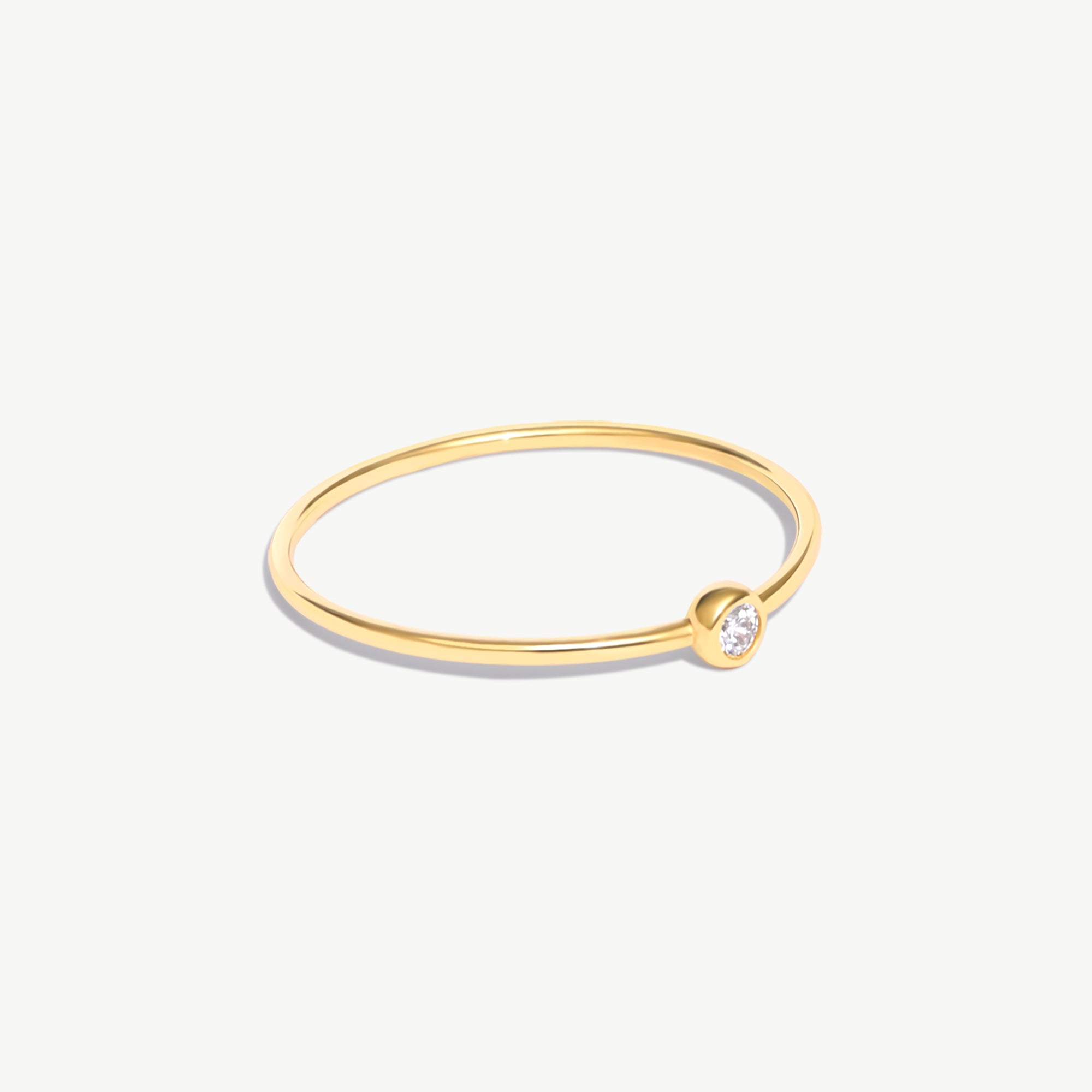 Side-angle product photograph of a delicate 14K solid gold birthstone ring with natural diamond bezel setting and ultra-thin minimalist band design.