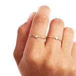 Close-up hand photo showing two dainty stackable 14K solid gold rings including a natural diamond birthstone ring paired with a minimalist heart ring in elegant everyday styling.