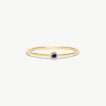 Minimalist 14K solid gold birthstone ring featuring a natural blue sapphire gemstone in a bezel setting on a delicate thin gold band photographed on a white background.