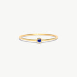 Minimalist 14K solid gold birthstone ring featuring a natural blue sapphire gemstone in a bezel setting on a delicate thin gold band photographed on a white background.