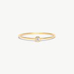 Fine jewelry product image of a delicate 14K solid gold birthstone ring with a natural diamond center stone and polished ultra-thin minimalist band photographed on a white background.