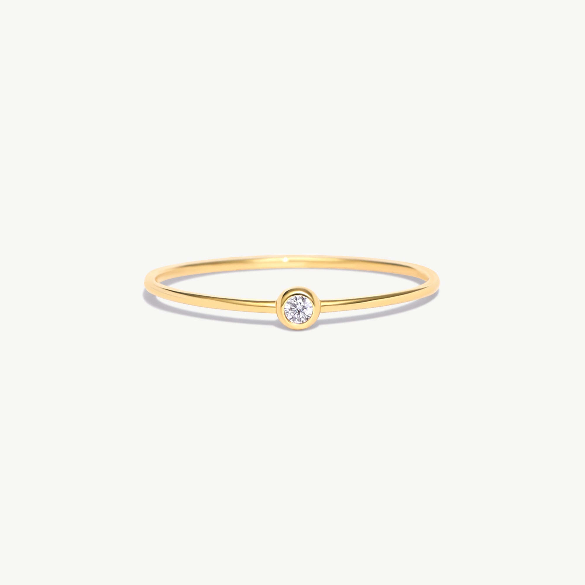 Fine jewelry product image of a delicate 14K solid gold birthstone ring with a natural diamond center stone and polished ultra-thin minimalist band photographed on a white background.