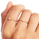 Lifestyle close-up of a woman wearing a natural diamond birthstone ring stacked with a minimalist heart ring crafted from genuine 14K solid gold in warm editorial lighting.