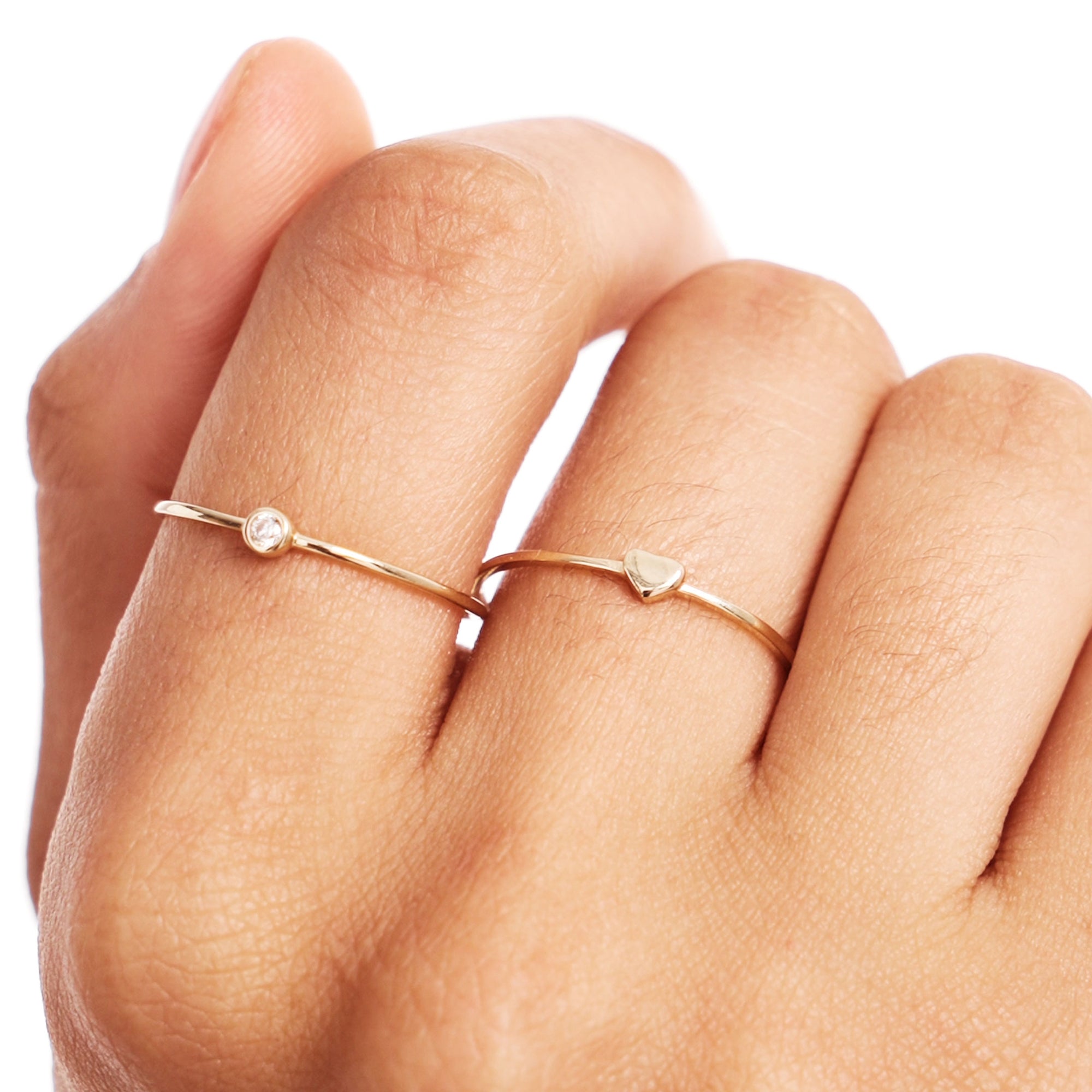 Lifestyle close-up of a woman wearing a natural diamond birthstone ring stacked with a minimalist heart ring crafted from genuine 14K solid gold in warm editorial lighting.
