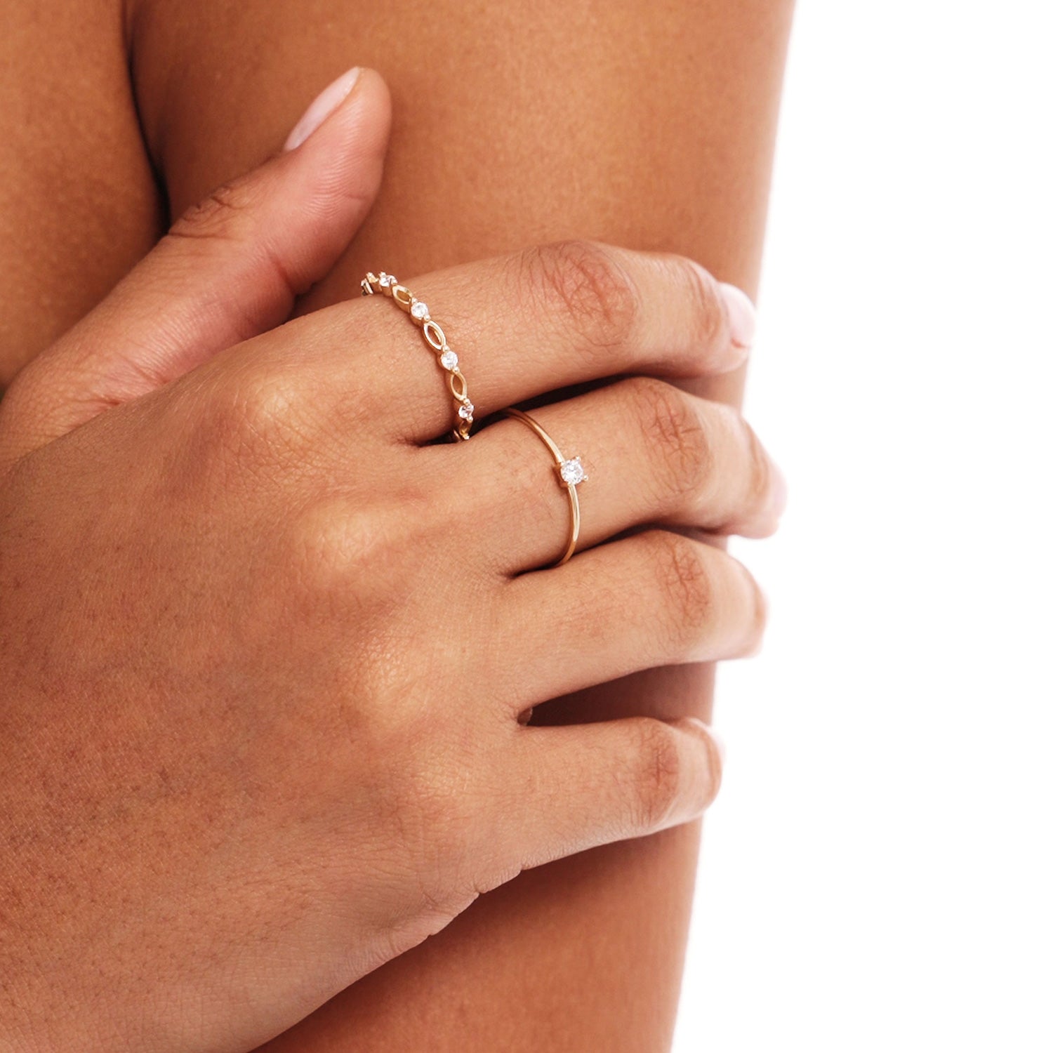 Close-up lifestyle photograph of a woman wearing delicate stackable 14K solid gold rings including a minimalist solitaire diamond engagement ring.