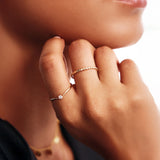 Lifestyle close-up of a woman wearing stackable 14K solid gold rings including a delicate diamond wishbone promise ring paired with a minimalist beaded gold band.