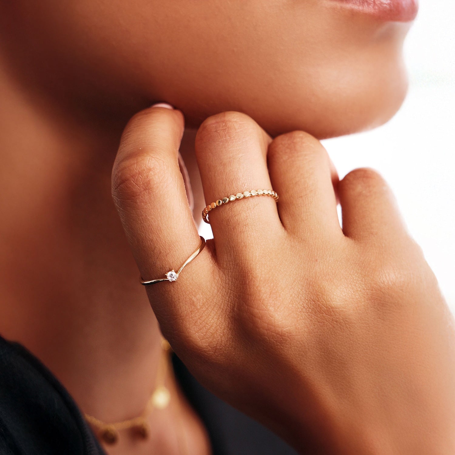 Lifestyle close-up of a woman wearing stackable 14K solid gold rings including a delicate diamond wishbone promise ring paired with a minimalist beaded gold band.