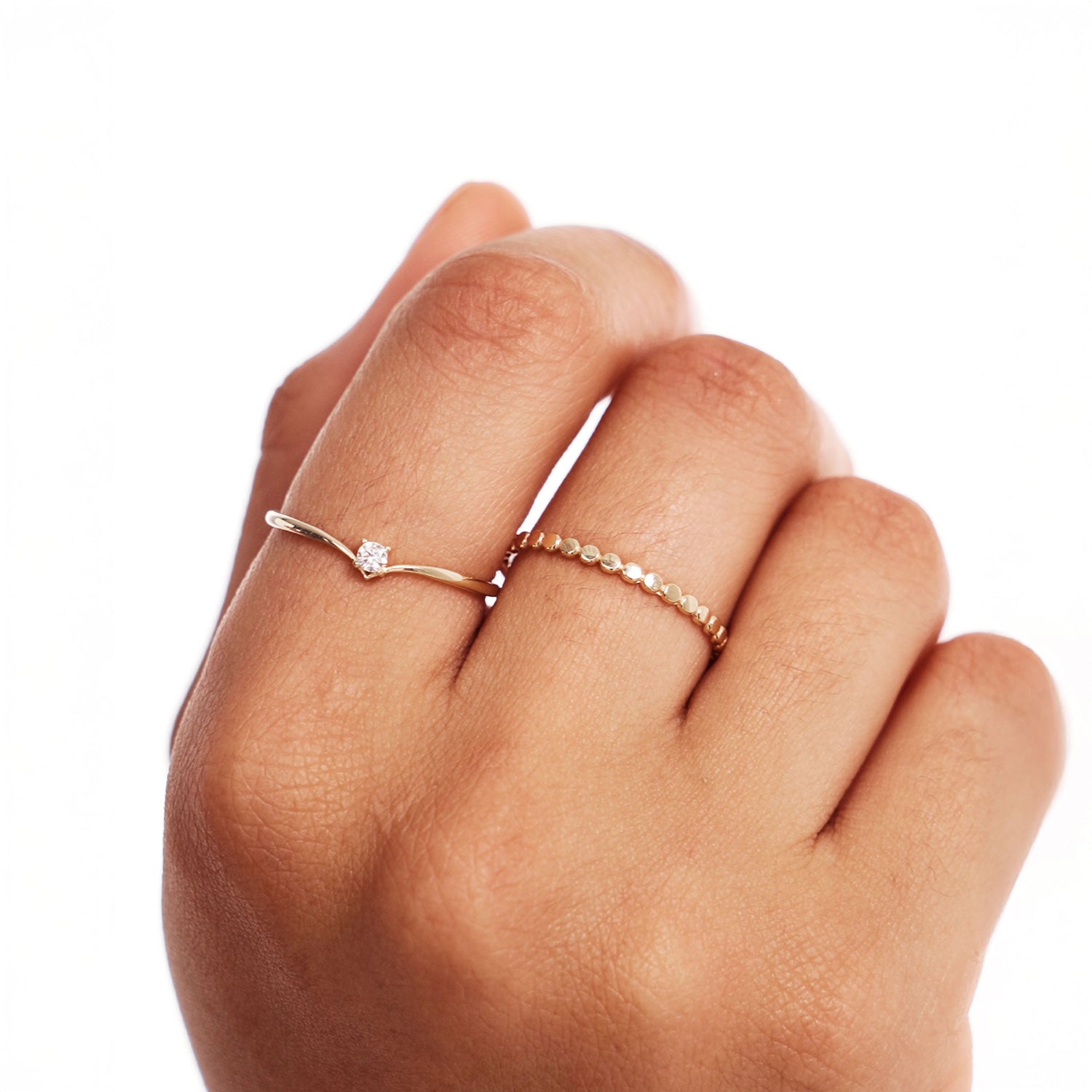 Close-up hand photograph showing a minimalist natural diamond wishbone ring stacked with a delicate gold beaded ring in elegant everyday styling.