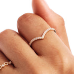 Close-up hand photograph showing a natural diamond wishbone wedding band worn as a minimalist stacking ring in warm natural lighting.