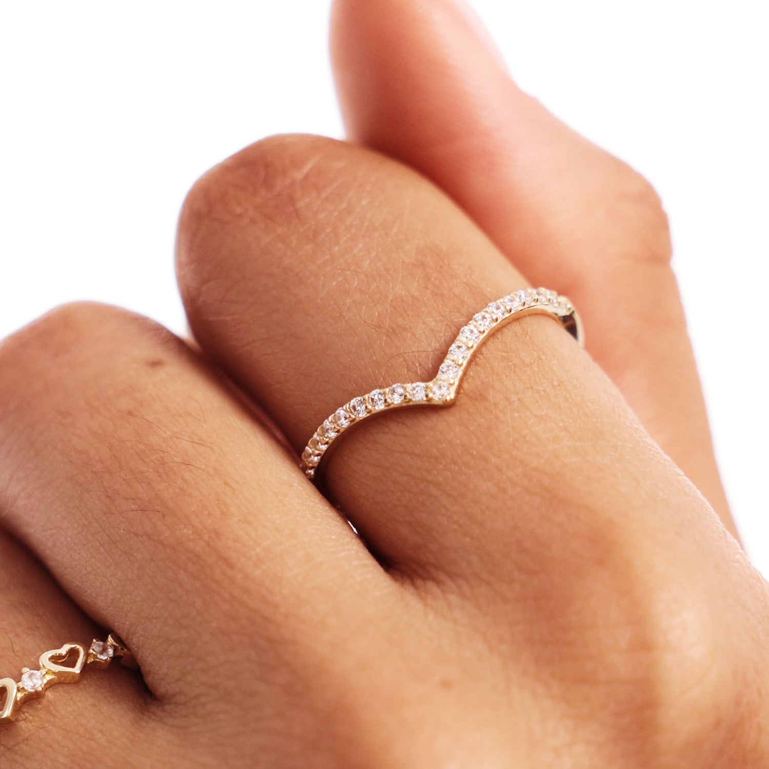 Close-up hand photograph showing a natural diamond wishbone wedding band worn as a minimalist stacking ring in warm natural lighting.