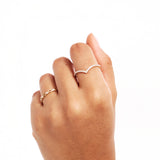 Editorial hand image featuring a minimalist pavé diamond V shaped ring stacked with other fine gold jewelry pieces for an elegant layered look.