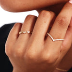 Luxury jewelry styling photograph showing a woman wearing a 14K solid gold eternity diamond wishbone band paired with delicate 14K solid gold heart ring with diamonds.