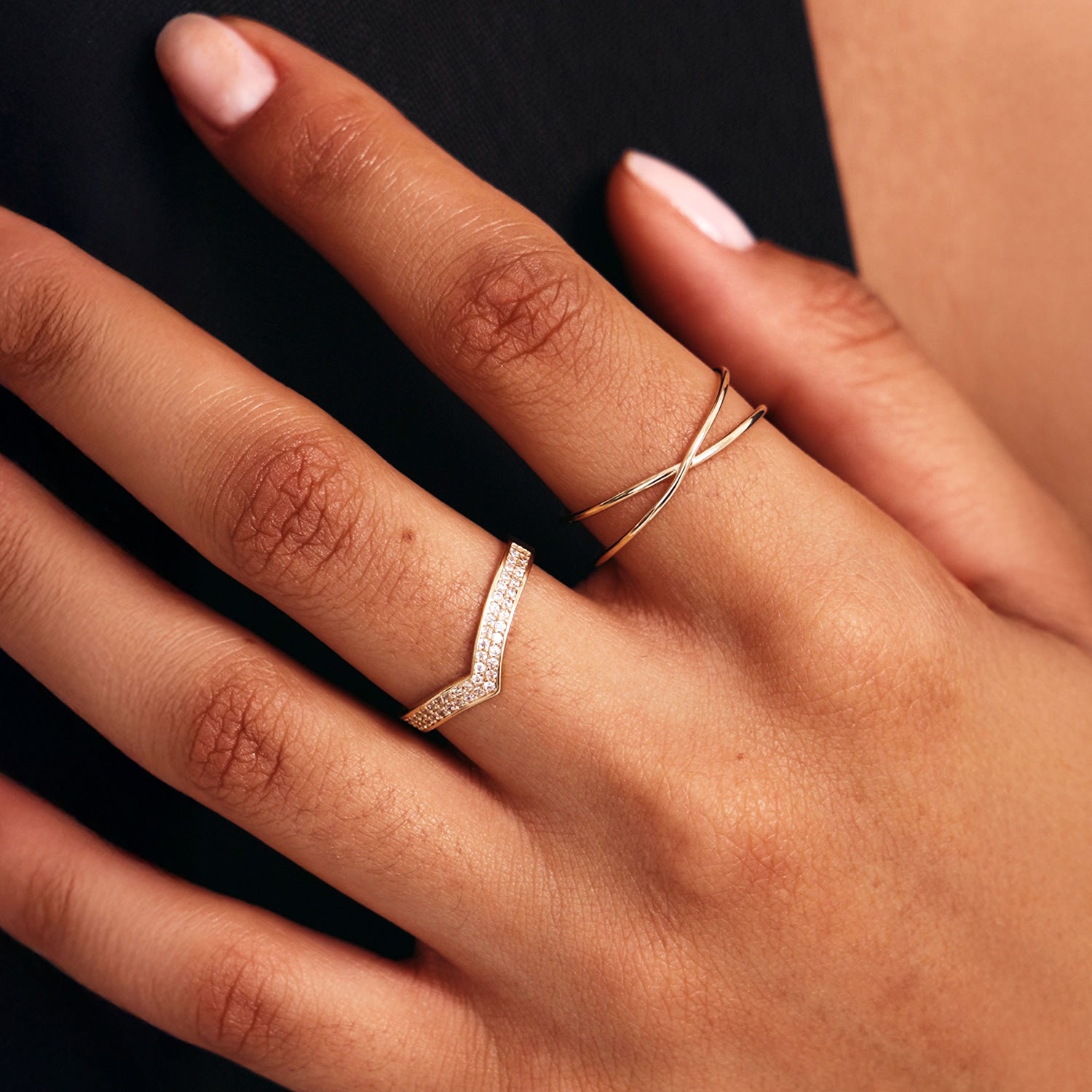 Lifestyle hand photograph featuring a minimalist 14K gold wishbone wedding band with pavé diamonds and a 14K Solid gold crossover ring.