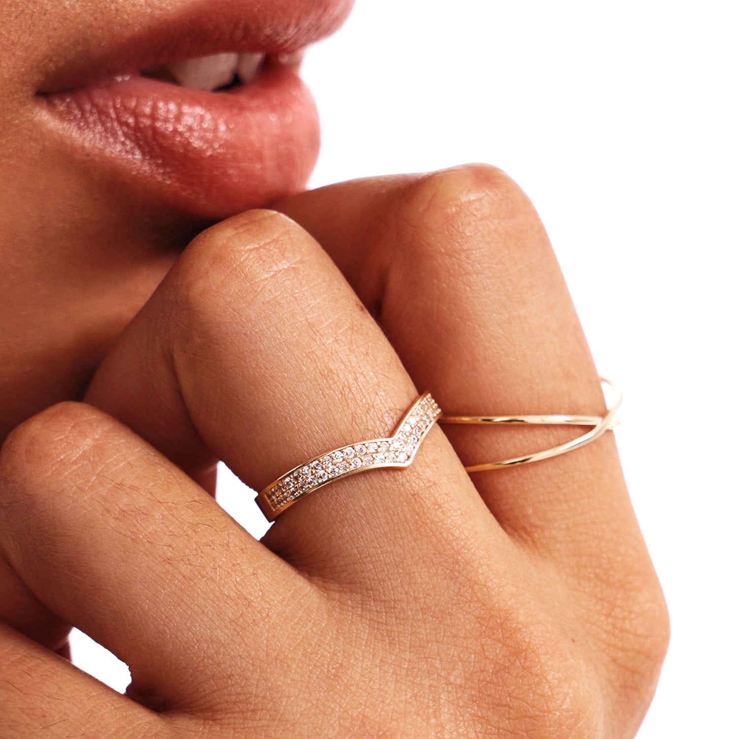 Close-up lifestyle image showing a pavé diamond V shaped promise ring stacked with a minimalist crossover gold ring on a woman’s hand.