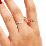 Close-up hand image showing a delicate diamond wishbone wedding band worn as a minimalist stacking ring beside a polished gold ring.
