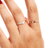 Close-up hand image showing a delicate diamond wishbone wedding band worn as a minimalist stacking ring beside a polished gold ring.