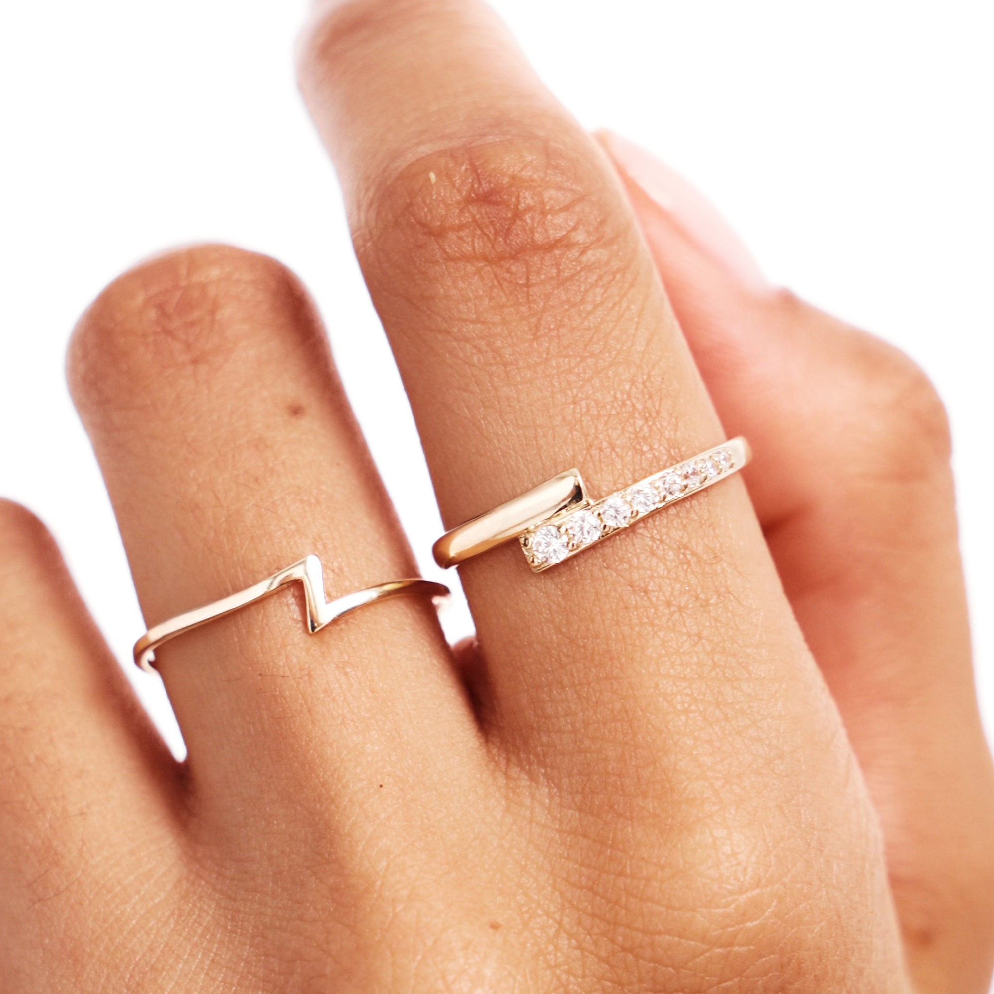 Hand styling photograph featuring a yellow gold lightning bolt ring layered with a diamond eternity band for a modern stacked ring look.