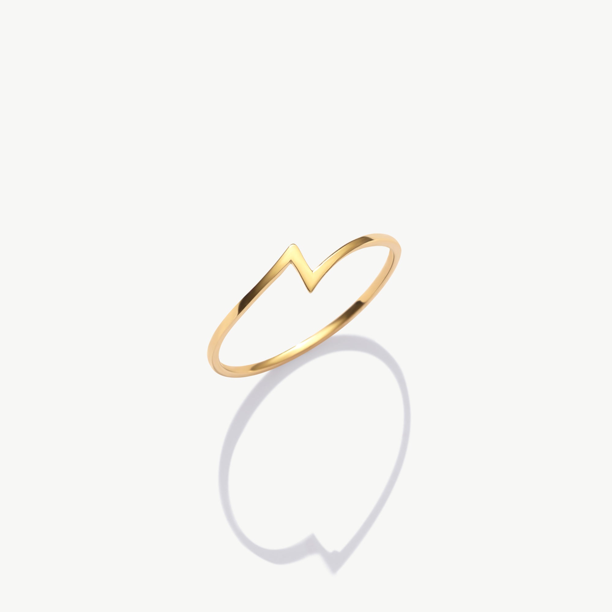 Minimalist yellow gold thunder bolt ring photographed upright on a white background with a soft shadow reflection.