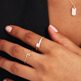 Editorial hand photograph featuring a rose gold lightning bolt ring paired with minimalist diamond rings and layered jewelry styling.