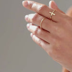 A cinematic luxury jewelry video showcasing a delicate 14K solid gold cross ring worn on a woman’s hand. The ring features a minimalist polished gold band with a small elegant cross detail centered on the top. Close-up macro shots capture the reflective gold texture, fine craftsmanship, and realistic sparkle under soft natural lighting. The model slowly moves her fingers and hand in a graceful editorial style, creating subtle gold reflections and shadows. Neutral luxury tones, clean manicure, soft skin text